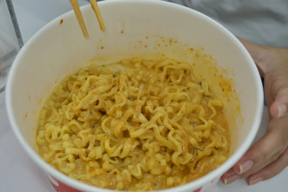 A paper bowl of spicy Buldak-style instant noodles with chopsticks, cooked at a self-serve ramyeon shop in Busan.