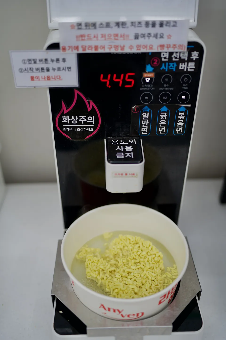 Self-serve instant ramyeon cooker in a Busan shop, with a bowl of noodles cooking and a 4:45 timer.