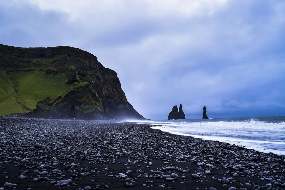 The black pebble beach at Reynisfjara near Vík, with a grassy headland and the Reynisdrangar sea stacks offshore