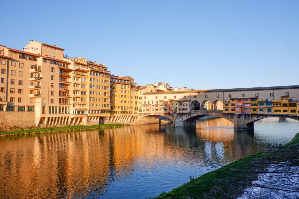 Ponte Vecchio and the Arno in Florence at golden hour, with the bridge reflected in the water
