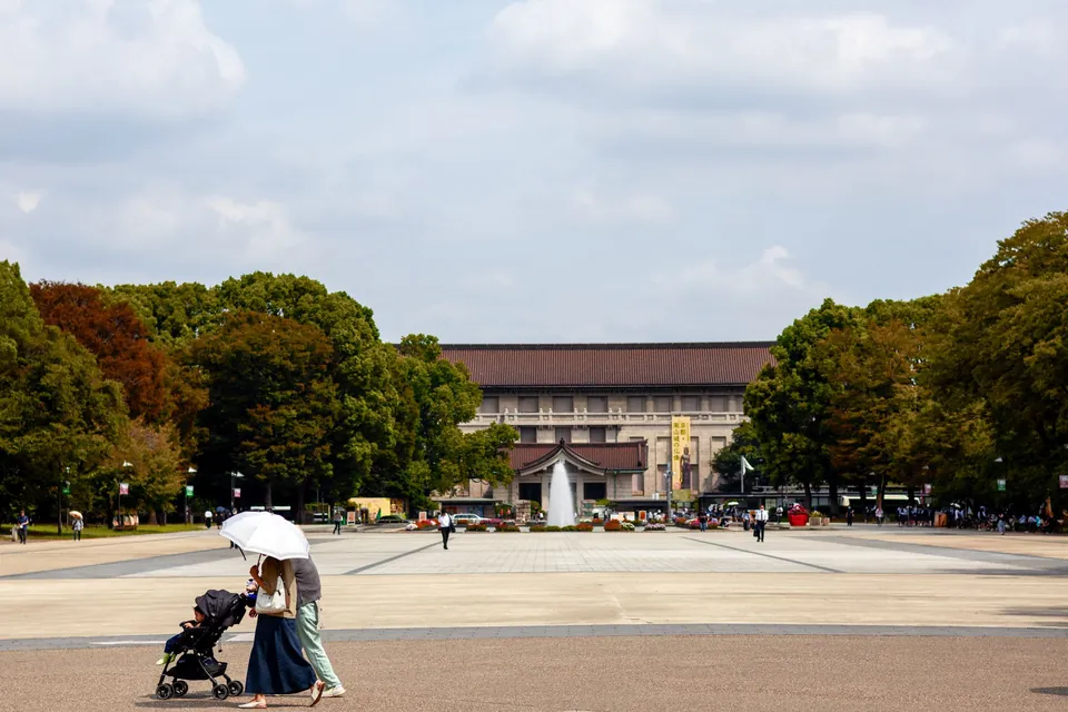 A parent pushing a stroller across the wide plaza of Ueno Park in Tokyo, with the Tokyo National Museum behind