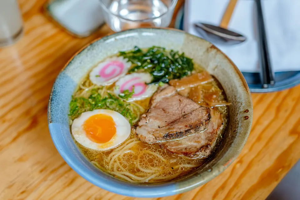 A bowl of ramen with sliced pork, a soft-boiled egg and spring onions