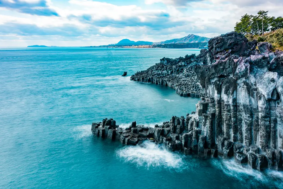 Columns of dark volcanic basalt dropping into turquoise sea on Jeju's south coast near Seogwipo