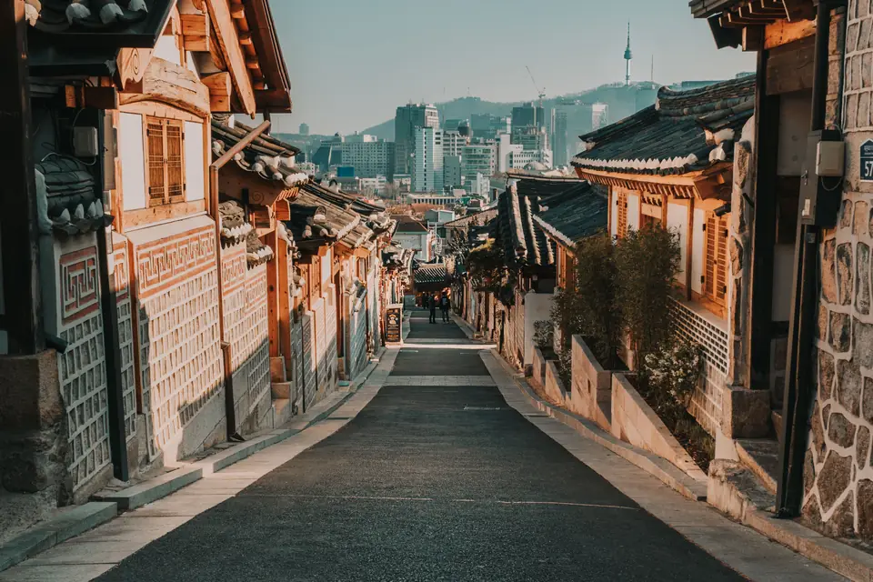 A quiet lane of tiled hanok houses in Bukchon, with Seoul's towers and N Seoul Tower in the distance