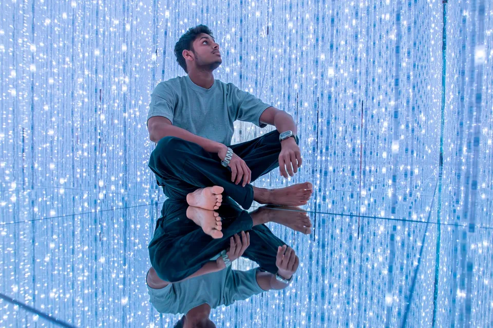A man sitting barefoot on a mirrored floor among hanging strings of light at teamLab Planets in Tokyo