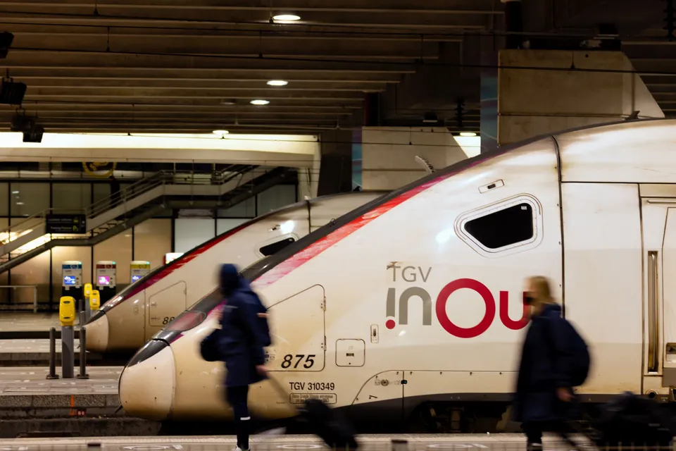 Travellers walking past TGV INOUI trains at a platform in Paris