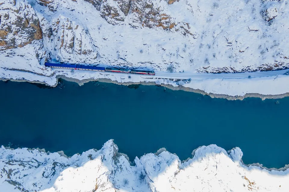 An Eastern Express train on the Ankara to Kars line, running beside a river under snowy cliffs near Kemah